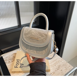 Close-up of light blue saddle bag featuring crinkled metallic leather and gold bar detail