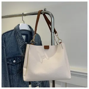 Dettaglio della borsa tote in pelle litchi bianco sporco con manici marroni e catena oro