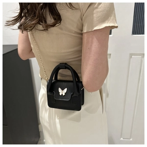 Detail of a black mini crossbody bag with a white butterfly ornament and gold chain strap