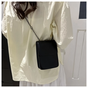 Close-up of a minimalist black leather cell phone crossbody bag with a matte chain strap