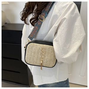 Detail of woven straw crossbody bag featuring gold logo, tassel, and ethnic strap