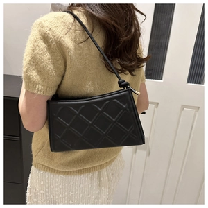 Rear view of a model wearing a black quilted leather shoulder bag with gold metal hardware
