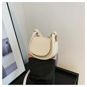 Close-up of minimalist cream mini saddle bag featuring round silhouette and decorative strap