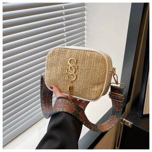 Close-up of woven straw crossbody bag with golden logo, tassel detail and ethnic strap
