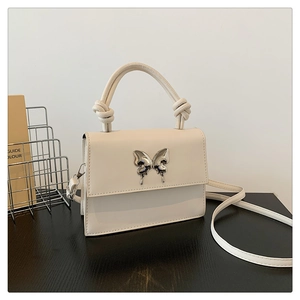 Détail du sac à main crème avec boucle papillon argentée et poignée à nœud tressé