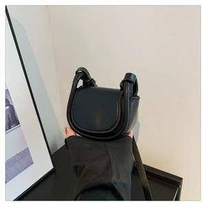Handheld view of a mini black vintage saddle bag featuring smooth faux leather texture