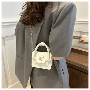 Close-up of white mini handbag with gold butterfly clasp and chain strap on model