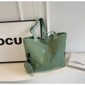 Close-up of green canvas tote bag featuring colorful embroidery and detachable coin purse