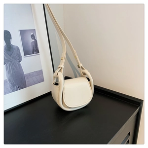 Detail view of cream mini saddle bag with smooth leather finish and gold hardware