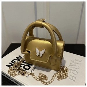 Macro shot of metallic golden mini bag with white butterfly clasp and chain strap