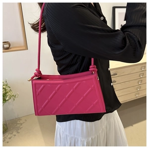 Detail of a magenta underarm bag with quilted diamond pattern and knotted leather strap