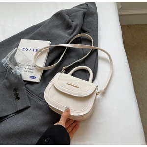 Close-up of minimalist cream saddle bag with marble textured flap and gold metal bar