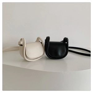 Detail view of mini matte leather saddle bags in cream and black with flap closure