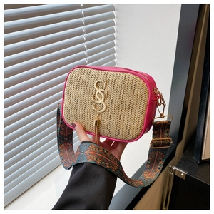 Close-up of woven straw handbag with rose red leather trim and ethnic pattern strap