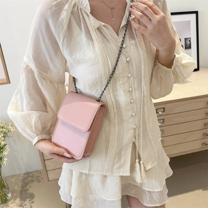Pink crossbody phone bag with chain strap shown in a cozy indoor home setting