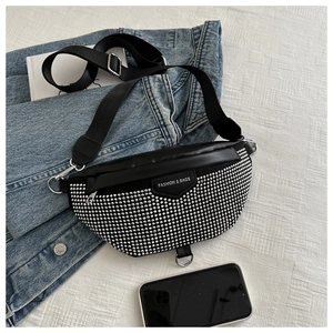 Détail du sac banane en cuir noir avec rivets argentés sur une veste en jean bleu