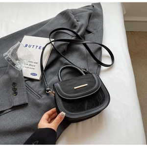 Detail of black crossbody saddle bag with marble texture flap and gold hardware