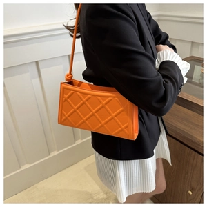 Detail view of an orange quilted shoulder bag showing the textured diamond pattern texture
