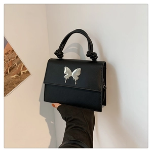 Détail d'un petit sac carré noir avec papillon argenté et poignée à nœud élégante
