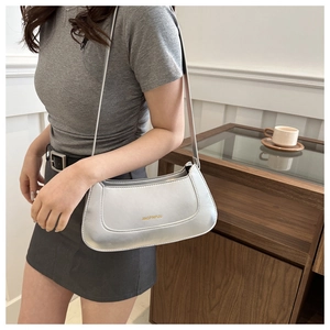 Detail of a silver metallic baguette shoulder bag showing the golden logo and texture