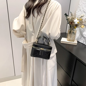 Chic black quilted crossbody bag with gold chain strap shown on model in cream coat