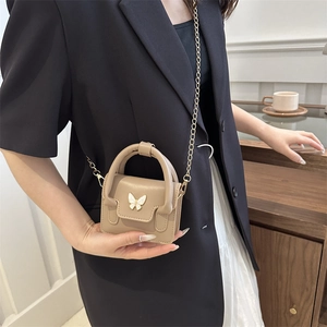 Beige mini crossbody bag with gold butterfly hardware and elegant chain strap on model