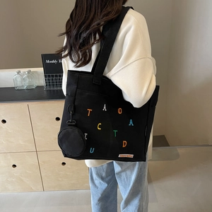 Cabas noir en toile avec broderie colorée et mini pochette porté par un mannequin