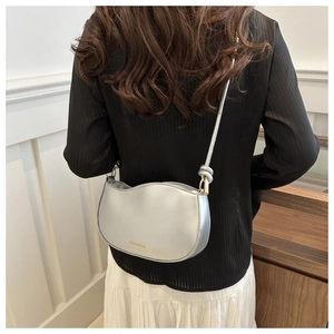 Silver metallic shoulder bag with knot detail worn by a model in a modern interior