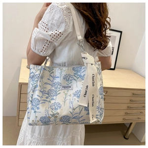Détail d'un sac cabas blanc à fleurs avec bandoulière en cuir et étiquette décorative
