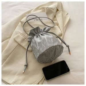 Macro shot of silver drawstring bucket bag with pleated metallic texture and gold hardware