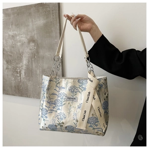 Détail d'un sac cabas à fleurs avec broderie bleue, chaîne en métal et étiquette logo