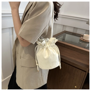 Detail of cream drawstring bucket bag with thin shoulder strap on a model indoors