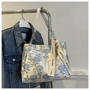 Détail de broderie florale sur tote bag beige avec chaîne argentée et ruban déco