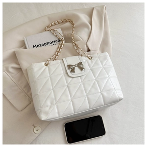 Detail of white quilted tote bag featuring a silver metal bow and golden chain strap