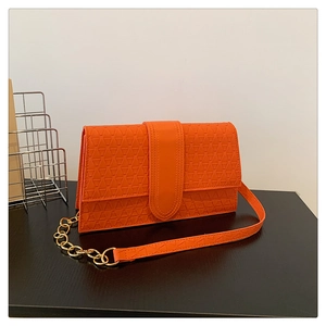 Détail d'un sac bandoulière orange en similicuir avec chaîne dorée et gaufrage géométrique