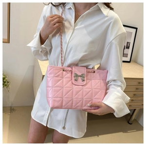 Detail of pink quilted shoulder bag with silver bow buckle and chain strap on model