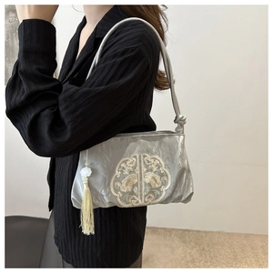 Detail of silver pleated shoulder bag featuring Chinese floral embroidery and white jade tassel