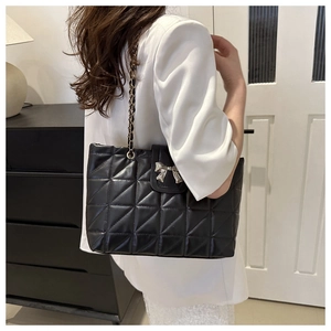 Close-up of quilted tote bag featuring silver bow buckle and gold chain strap detail