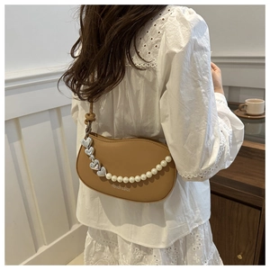 Close-up of caramel leather crescent bag with decorative pearl and heart chain detail