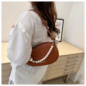 Detail of brown leather handbag featuring pearl chain strap and heart charm accents