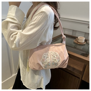 Pink silk shoulder bag with traditional embroidery and tassel detail on a model