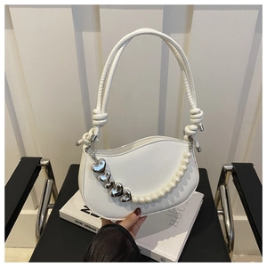 Detail of white half-moon bag featuring pearl chain and heart charms on a book