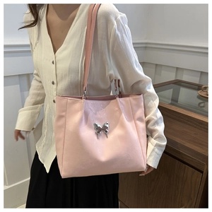 Détail du sac cabas rose pâle avec papillon métallique et texture en cuir brillant chic