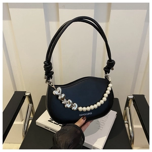 Detail of crescent moon bag with pearl and heart chain on a black leather surface