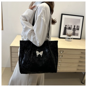 Détail du sac cabas noir brillant orné d'un papillon métallique argenté élégant