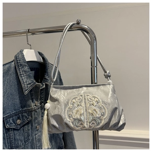 Detail of silk texture bag with floral embroidery and beige tassel hanging on a rack