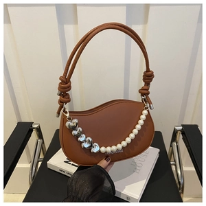 Detail of tan wavy handbag featuring pearl chain and silver heart charms on magazines