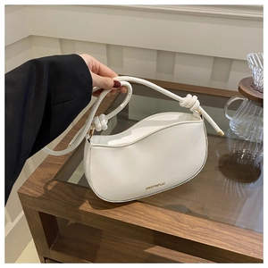 Close-up of white half-moon bag featuring a knotted handle and golden ring accents