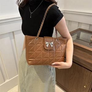 Brown quilted tote bag with silver bow detail and chain strap shown on shoulder