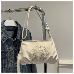 Close-up of elegant floral embroidery and white tassel detail on a textured cream bag